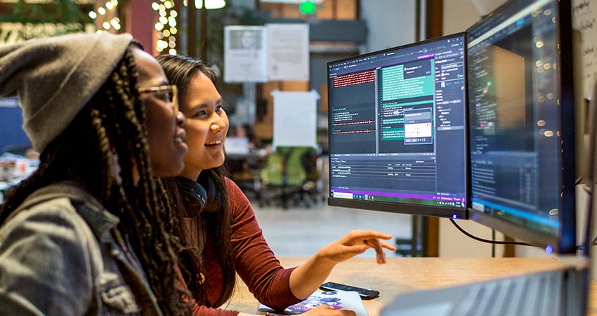 two people sitting next to each other looking at a computer screen