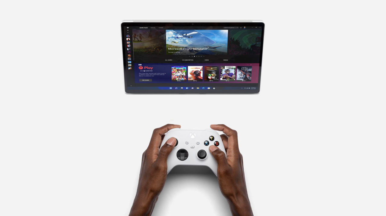 a pair of hands holding an Xbox controller in front of a tablet